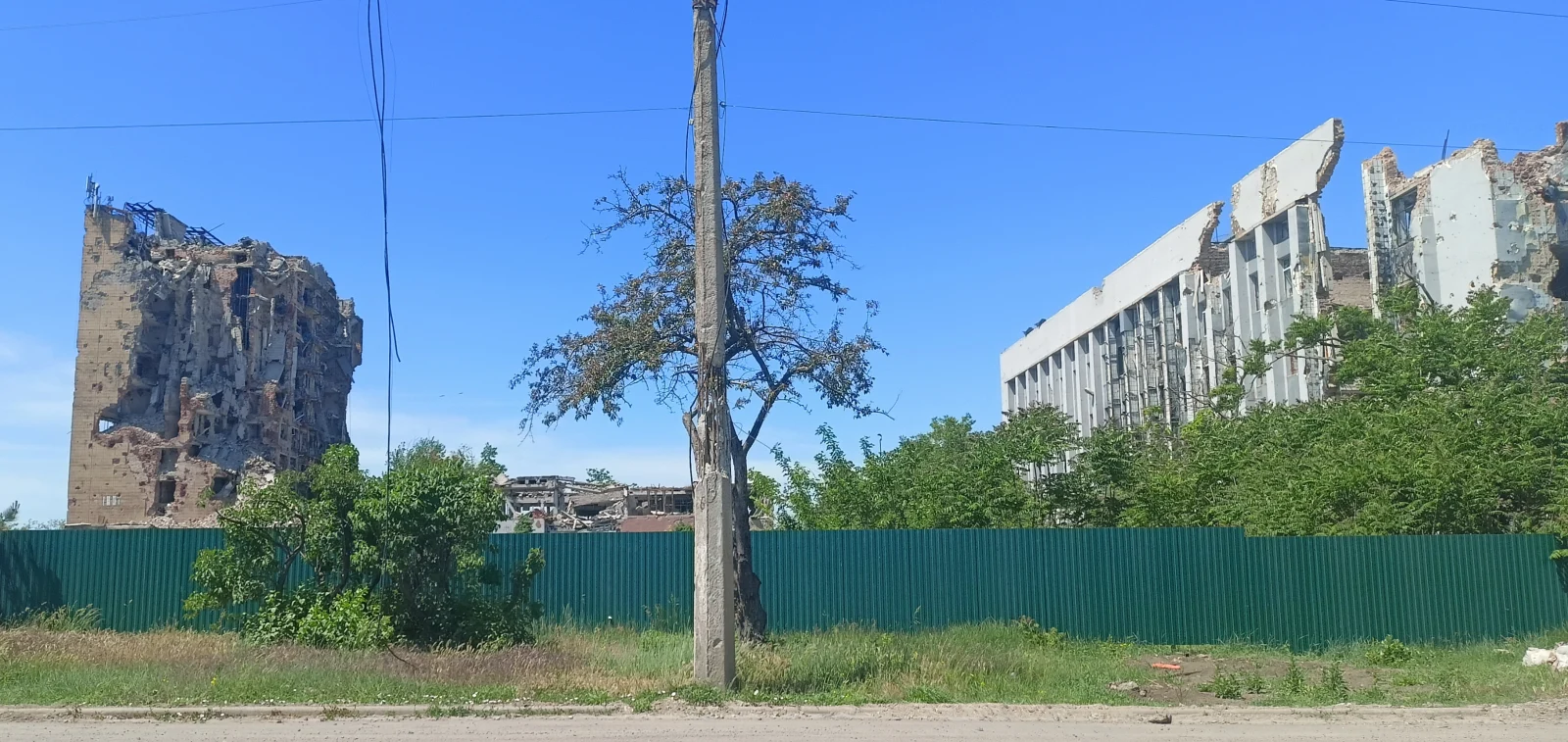 Ruinas de edificios administrativos del distrito de la margen izquierda de Mariúpol, detrás de una cerca verde, en una fotografía del 22 de mayo de 2024.
